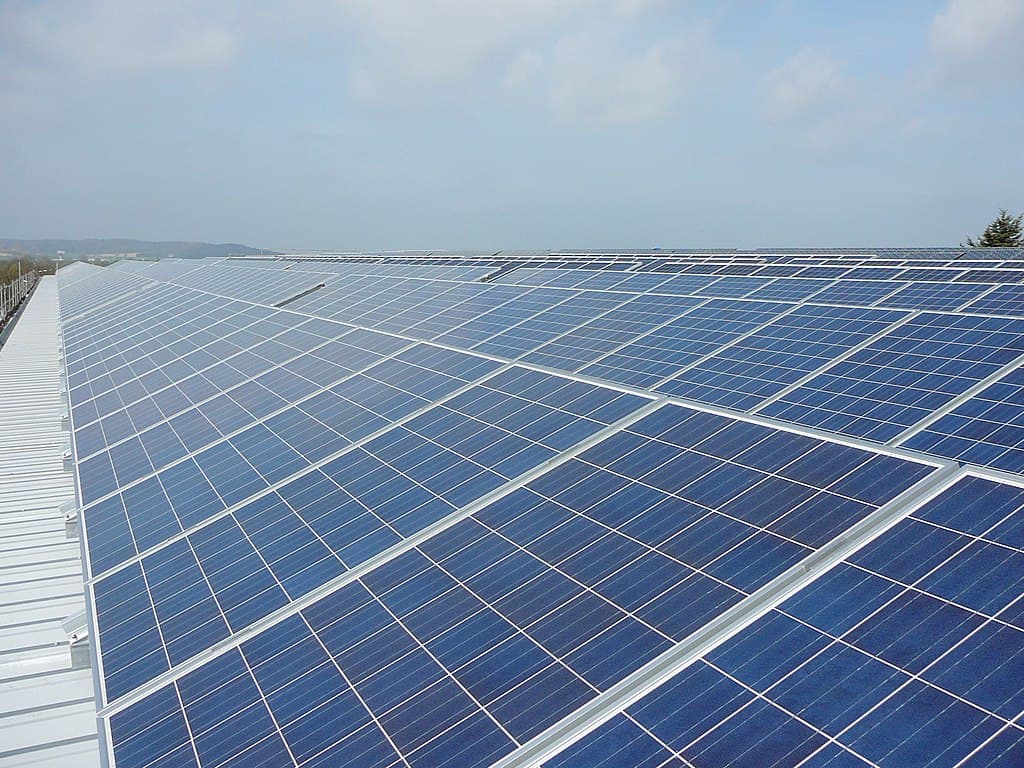 Aerial view of solar panels installed on a rooftop, showcasing a clean energy solution under a blue sky. The image highlights the rows of photovoltaic cells, emphasizing renewable energy technology and its role in sustainable living.