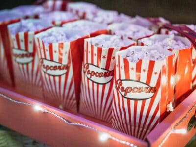 Colorful popcorn bags arranged neatly in a pink tray, illuminated by string lights, perfect for a movie night or party snack display.